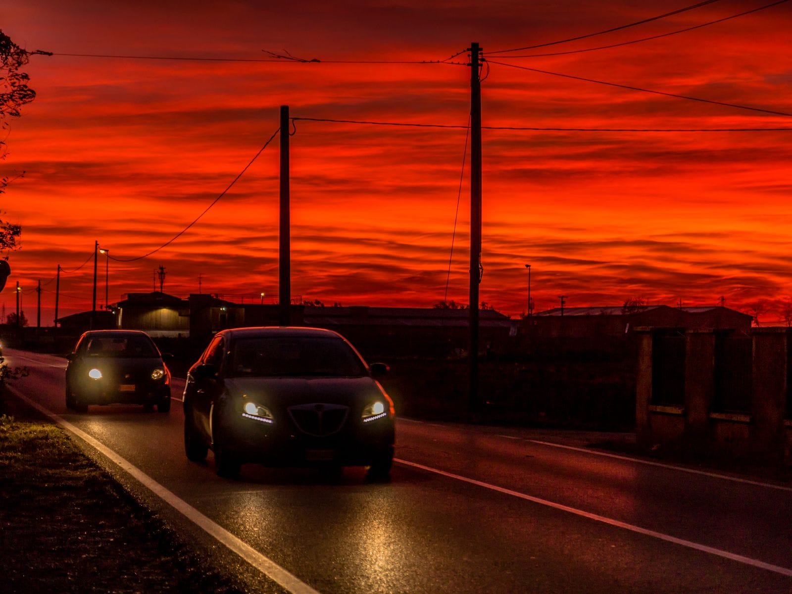 Two cars traveling on a road during a golden sunset.