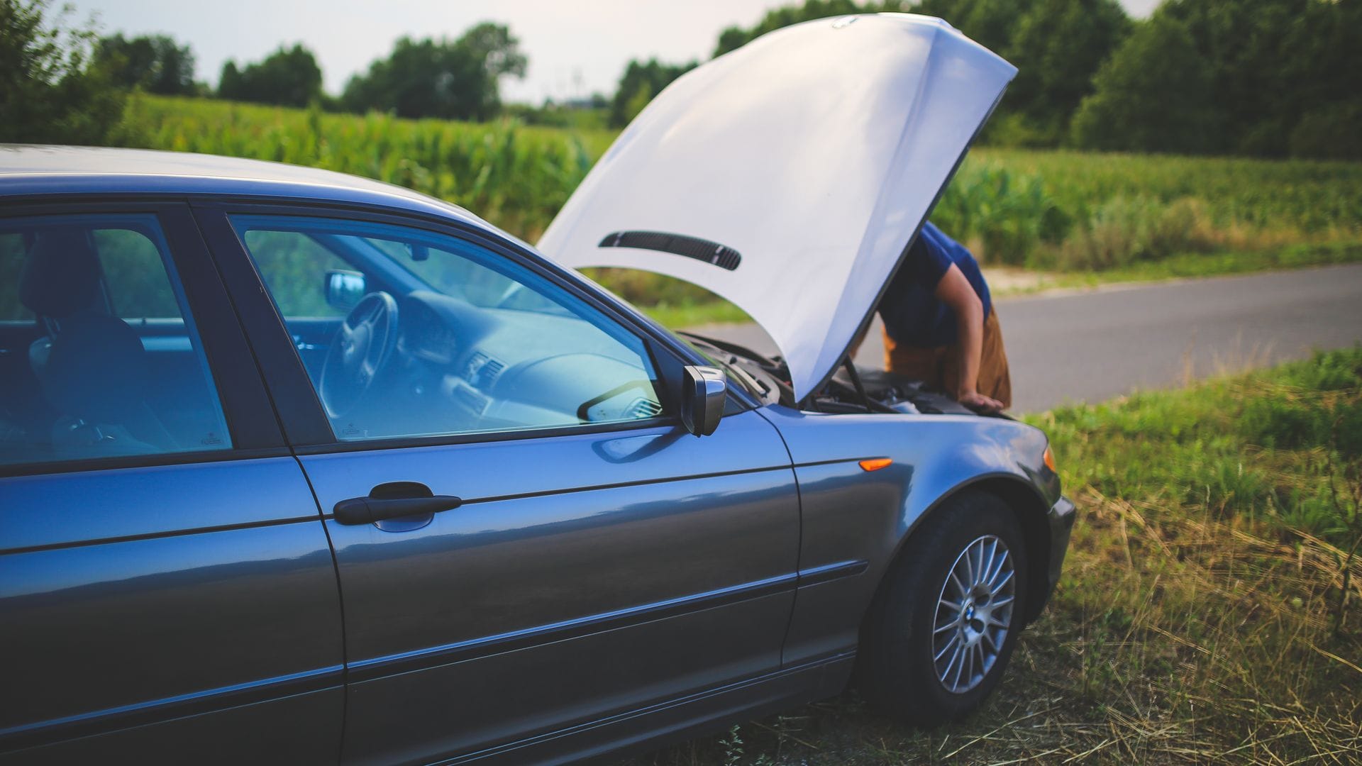 Driver checking a car engine beside a rural road